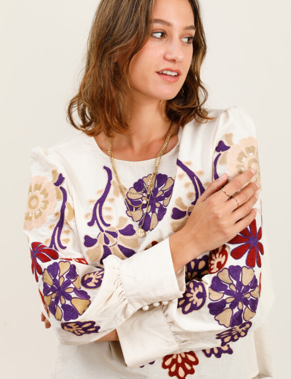 comprar Blusa en tono crudo con bordados folk en morado, granate y beige. Cuello redondo, manga abullonada con puño ancho y silueta relajada.
